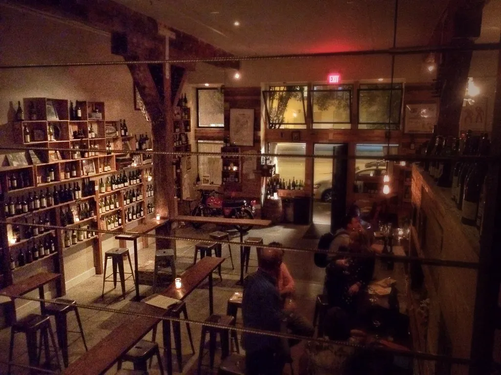 Innsiden av baren: hyller med vin, krakker og gjester, skumring i vinduene
